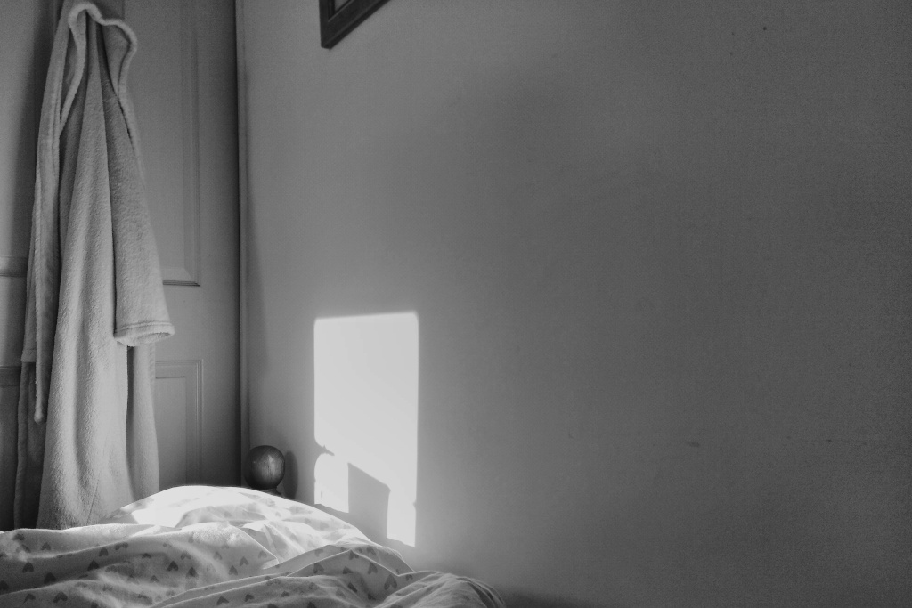 A square of light falls on a wall, alongside a dressing gown hanging from a door.