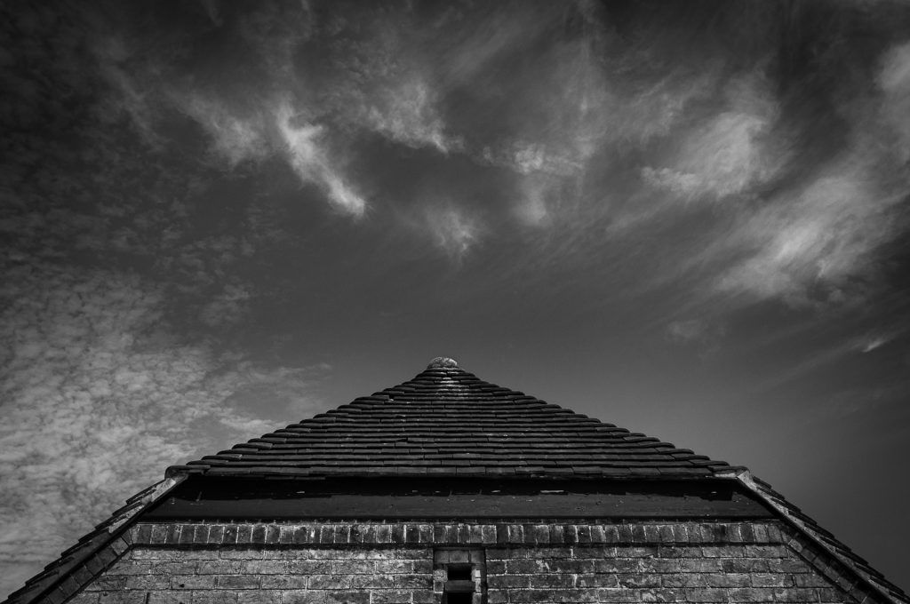 Black and white photo of a barn roof against a sky filled with clouds