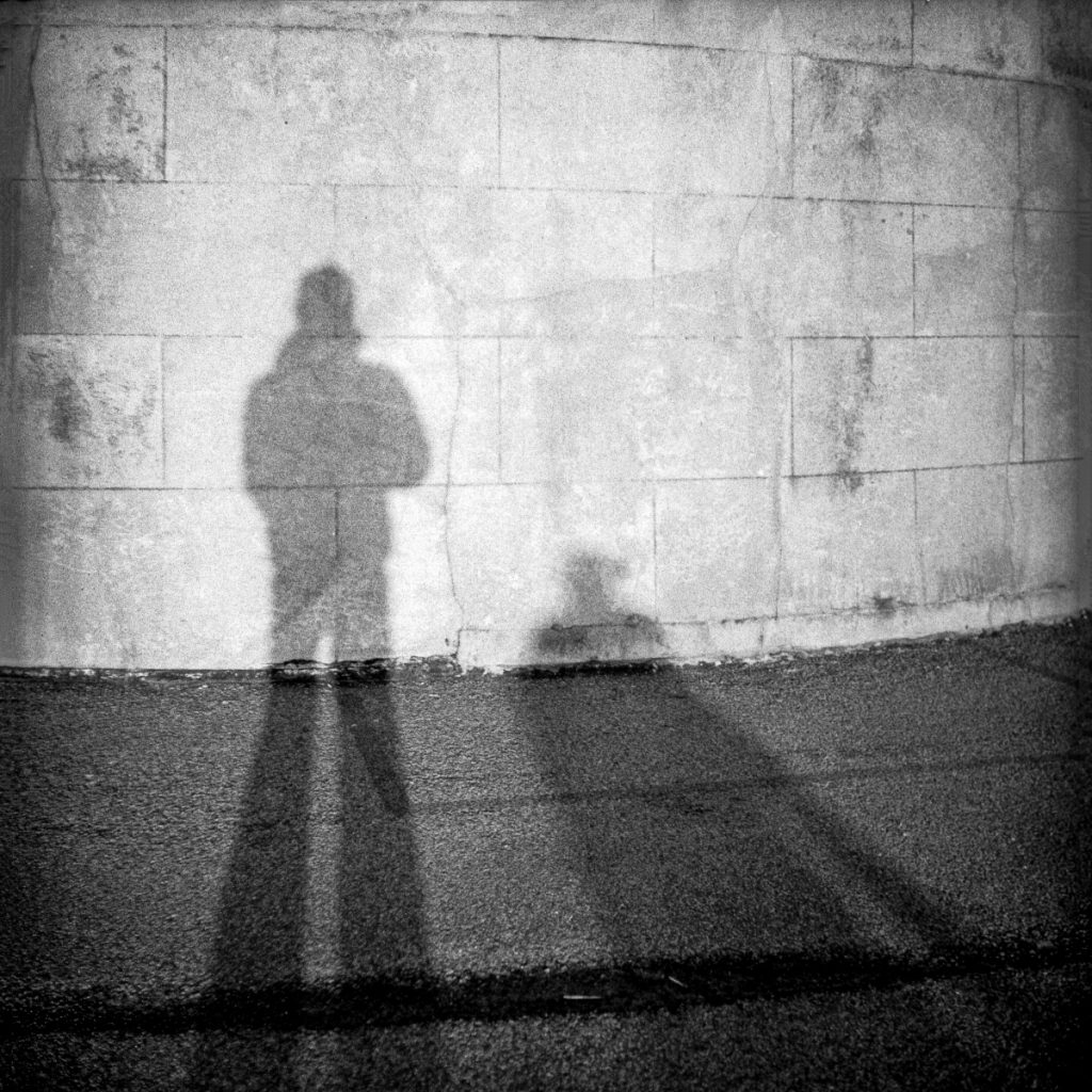 Elongated shadows of two people against a brick wall, black and white