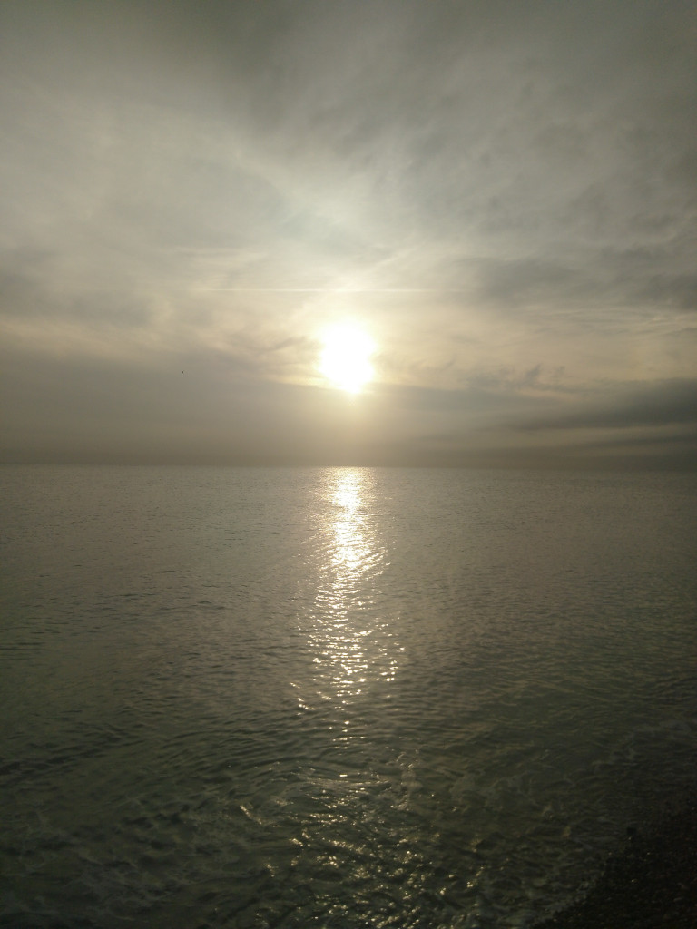 A pale sun going down over a calm sea