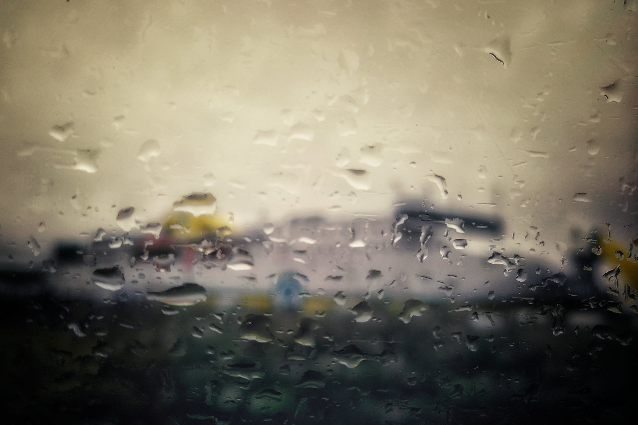 A large, rectangular white and yellow building-like structure is obscured by close up detail of raindrops on a window.